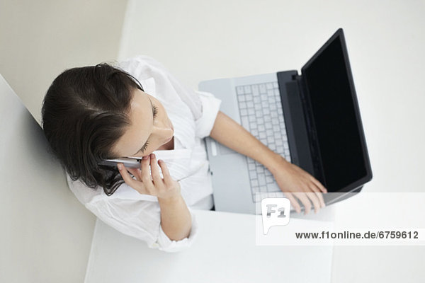 Woman talking on phone while holding laptop