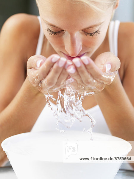 Frau spritzendes Wasser auf ihrem Gesicht