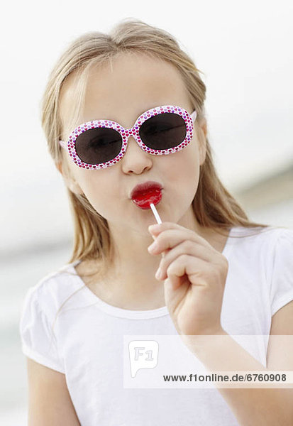 Girl (10-11) wearing sunglasses on beach is licking lollypop