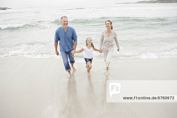Smiling family holding hands and walking on beach
