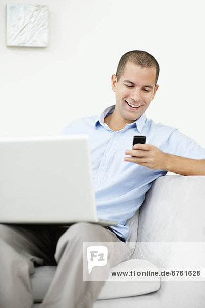 South Africa  Young man sitting on sofa with laptop and texting messages
