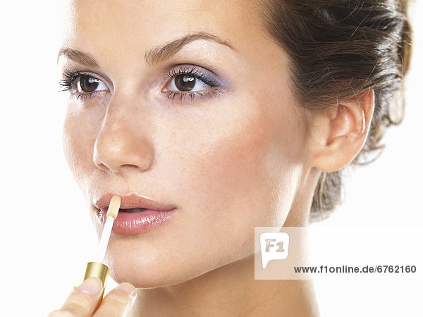 Studio portrait of beautiful woman applying lip gloss mouth