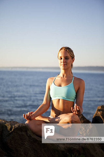 Athletic woman meditating by the ocean