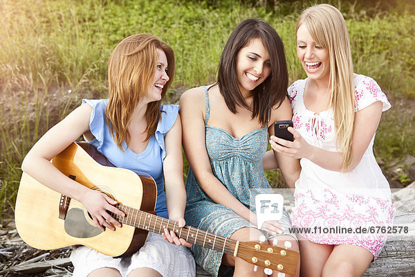 Three young women with guitar and cell phone relaxing