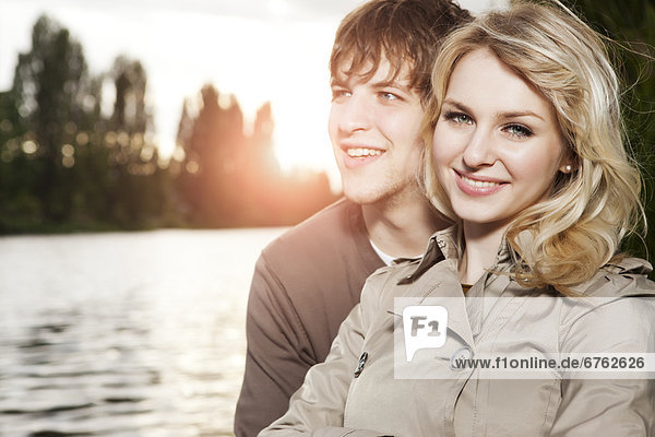 Portrait of young couple embracing by lake at sunset