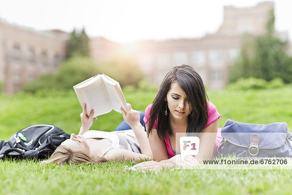 Two female college student lying on grass reading books