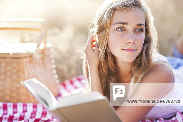 Teenage girl (16-17) taking break from reading book outdoors