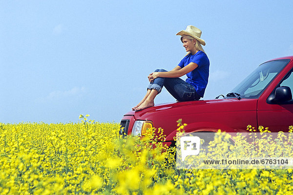 Teenager Sitting on a Red Pick Up Truck in a Canola Field  near St. Leon  Manitoba