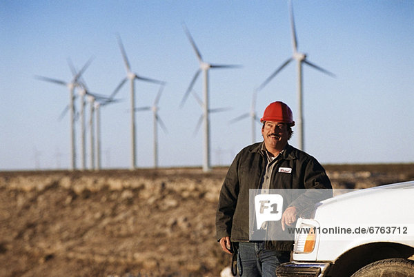 Worker leaning against truck with wind turbines in background