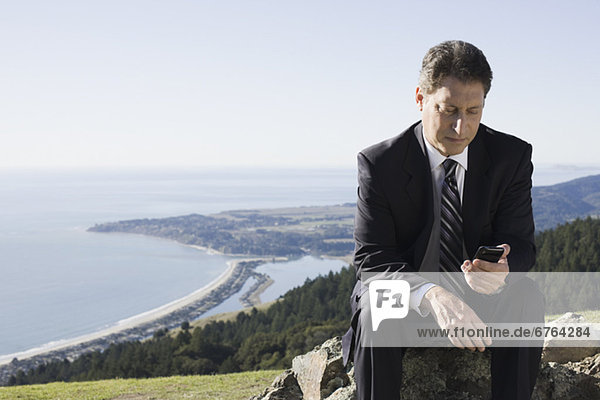 Businessman text messaging on remote hill