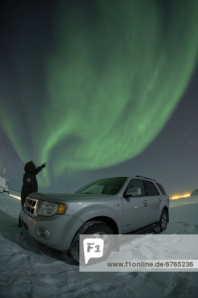 Observing aurora borealis (the Northern Lights) with the lights of the city of Yellowknife  Northwest Territories in the background.