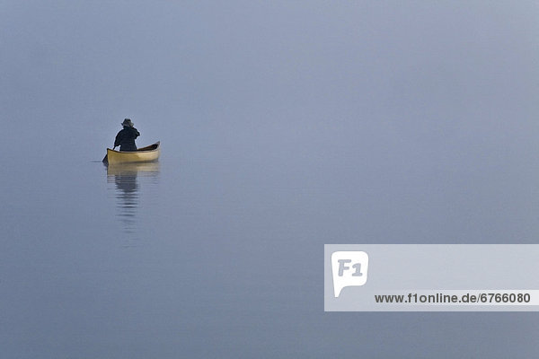 Woman paddling canoe in morning mist  Algonquin Park  Ontario