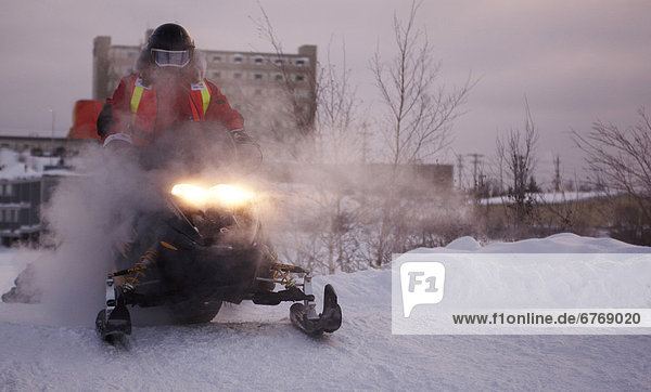 Snowmobiler cresting a small hill to come on to Frame Lake in downtown Yellowknife. Photographed at the Rock/Ice Ultra marathon in Yellowknife  Northwest Territories
