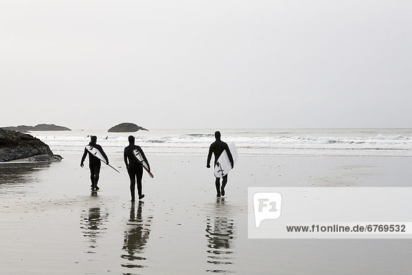 Three Surfers Walk on Beach Toward the Surf  Tofino  British Columbia