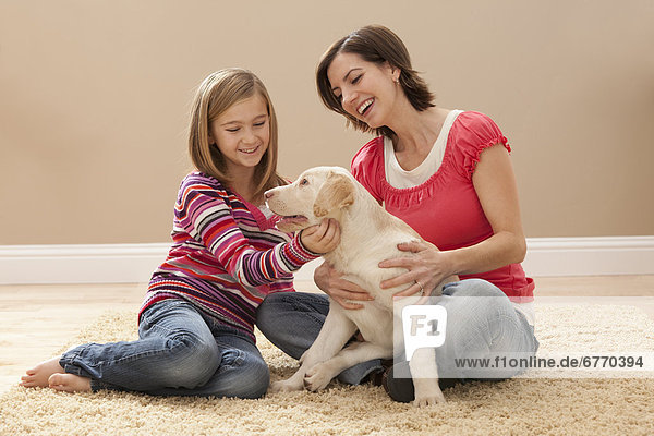Mother and daughter (10-11) playing with Labrador on carpet