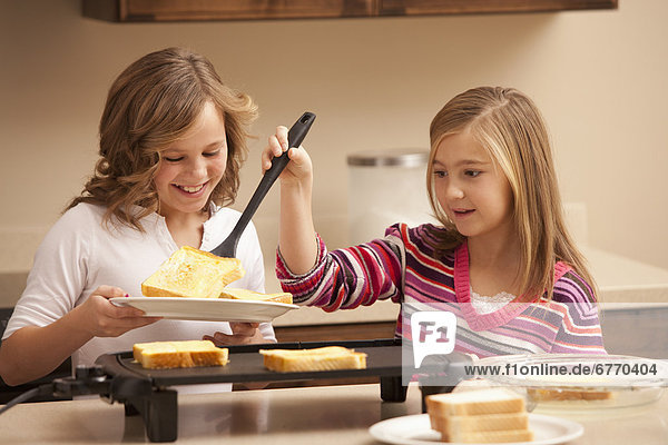 Two girls (10-11) preparing toast in kitchen