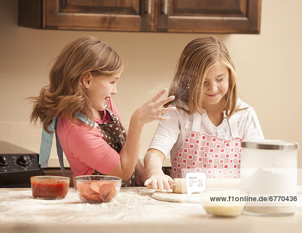 Two girls (10-11) preparing pizza in kitchen