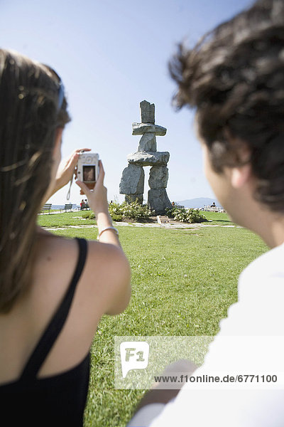 Couple taking a photo of an Inukshuk  along the Stanley Park Seawall  Vancouver  British Columbia