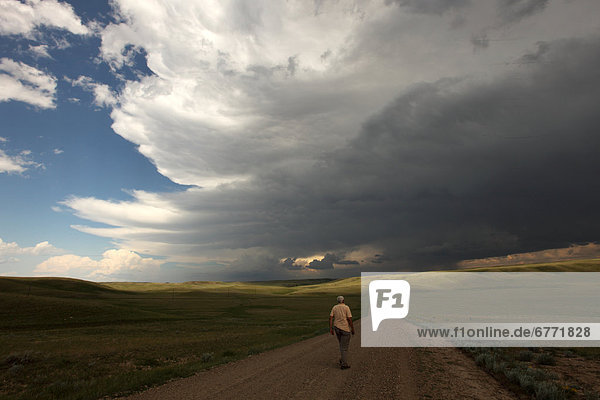Gentleman walking along ranch road while storm clouds gather overhead  Saskatchewan