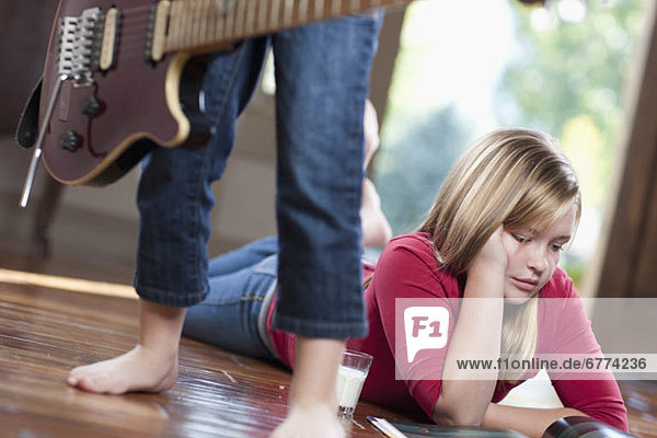 USA  Utah  Girl (10-11) reading magazine while another girl (6-7) playing guitar