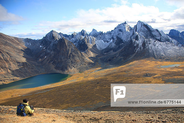 Hiker sitting on a mountain looking at Mount Monolith and Divide Lake in Tombstone Territorial Park  Yukon