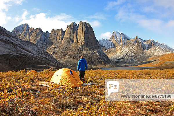 Camper standing by his tent at sunrise over Divide Lake with Mount Monolith in background  Yukon