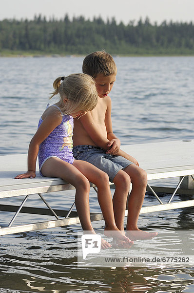 Brother and sister sitting on a lake dock looking into the water  Lac Sante  Alberta