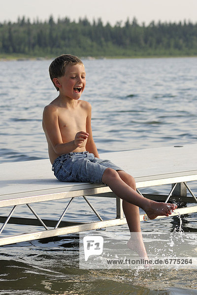 Young boy splashing his feet in the water on a lake dock  Lac Sante  Alberta