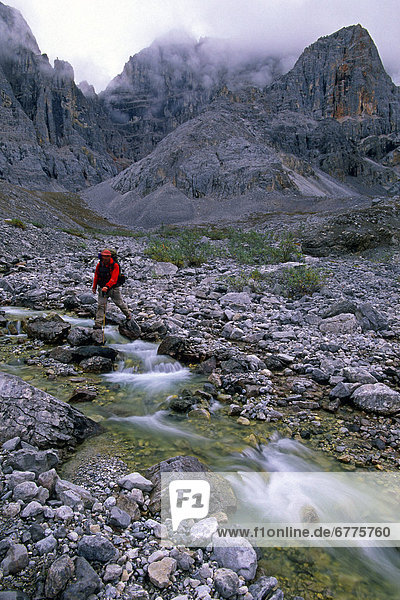 Hiker Crossing a Creek with cliffs of Mt. MacDonald in the background  Mayo  Yukon