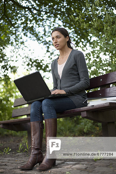 Young woman sitting on park bench using laptop
