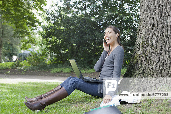 Handy  sitzend  benutzen  Frau  Notebook  Baum  unterhalb  jung
