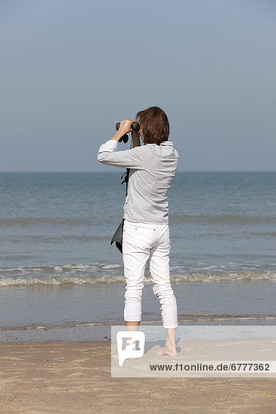 Woman on beach looking through binoculars