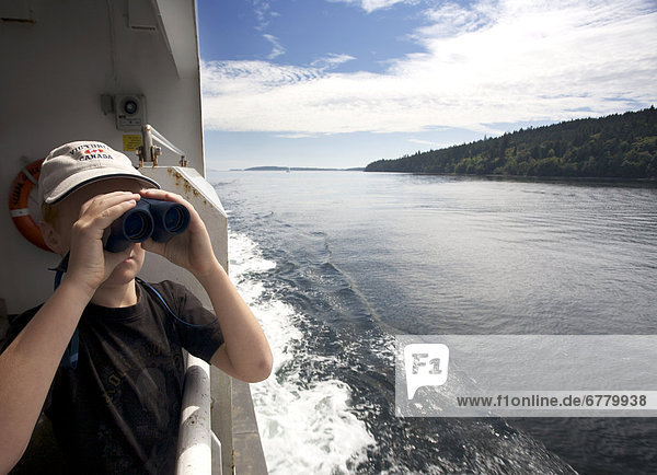 A young boy standing on a ferry  looks towards Salt Spring Island through binoculars  Gulf Islands  British Columbia