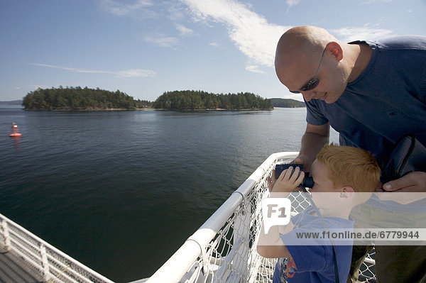 Father and son look through binoculars from the deck of the Salt Spring Ferry  Gulf Islands  British Columbia