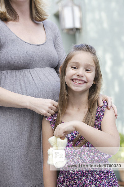 Pregnant mother standing with daughter (6-7) holding baby booties