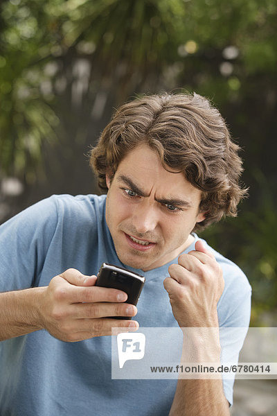 Young man text-messaging and shaking fist