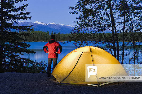 Hiker by a tent looking out at Boya Lake at dusk  Boya Lake Provincial Park  Northern British Columbia
