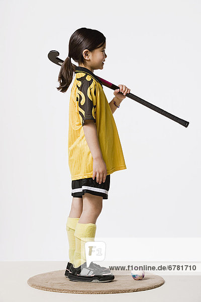 Studio portrait of girl (8-9) wearing sports clothes and holding hockey stick