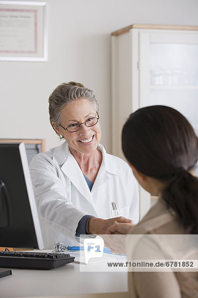 Smiling female doctor shaking hand with patient in her office