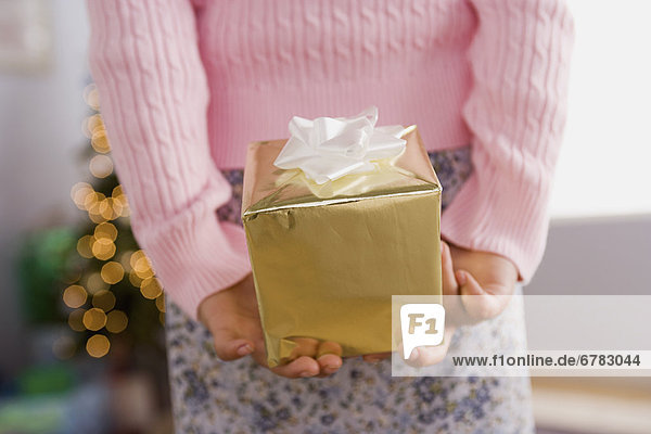 Close-up of girl holding Christmas present behind back  mid section