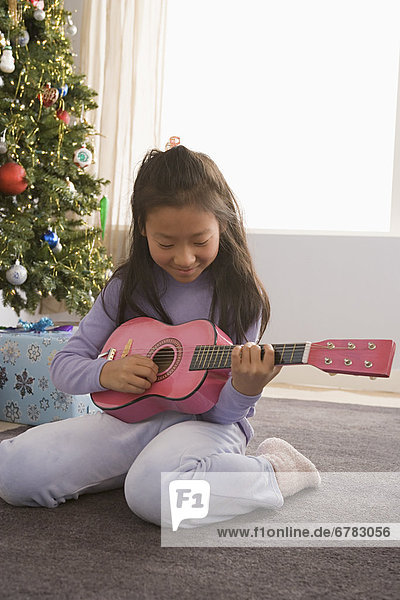 Girl (10-11) playing guitar  Christmas tree in background