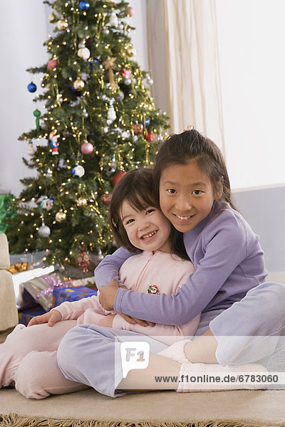 Portrait of two sisters (10-11) hugging at Christmas tree