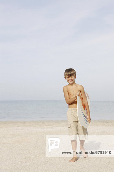 Portrait of boy holding bodyboard on beach