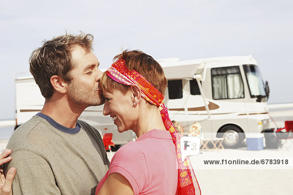 Couple kissing by motor home on beach