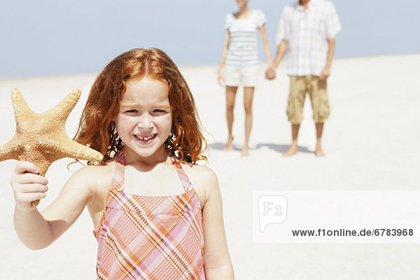 Girl holding up starfish on beach
