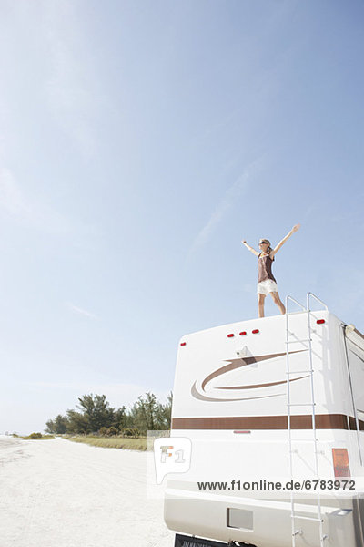 Woman standing on motor home with arms outstretched