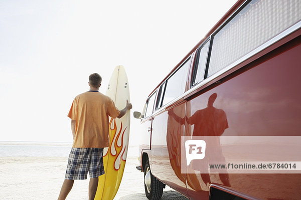 Man holding surfboard next to van on beach