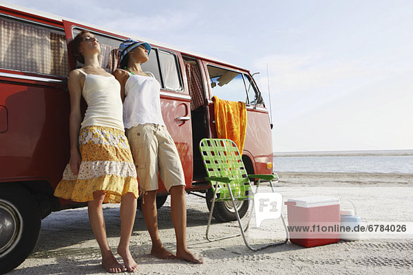 Young women leaning against van on beach