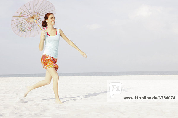 Girl running on beach with umbrella