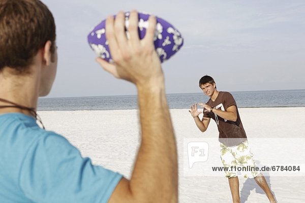 Friend playing football on beach